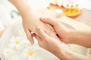 esthéticienne massant la main d'une cliente de salon de spa féminin. traitement de spa et produit pour les pieds féminins et le spa des mains. fleurs blanches dans un bol en céramique avec de l'eau pour l'aromathérapie au spa. photo