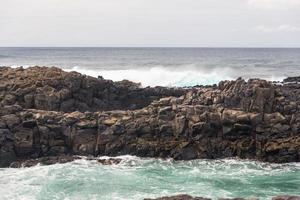 les vagues océaniques turbulentes avec de la mousse blanche battent les pierres côtières photo