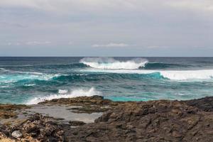 les vagues océaniques turbulentes avec de la mousse blanche battent les pierres côtières photo