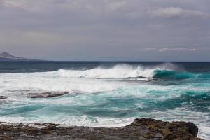 les vagues océaniques turbulentes avec de la mousse blanche battent les pierres côtières photo