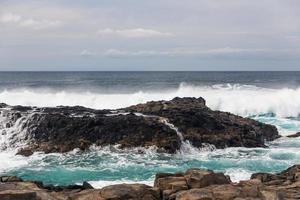 les vagues océaniques turbulentes avec de la mousse blanche battent les pierres côtières photo