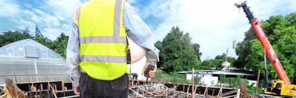 un ingénieur ou un ouvrier portant un gilet de sauvetage tient un talkie-walkie et une casquette blanche à la main. pour la sécurité de travail sur le fond du chantier de construction photo