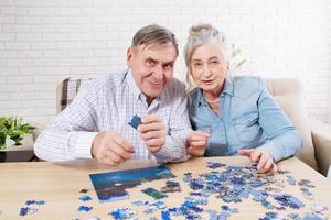 joli couple de personnes âgées résolvant un puzzle ensemble à la maison. photo