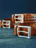 Trois ceintures en cuir marron foncé sur fond de bois photo