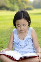 petite fille asiatique lisant un livre dans le parc photo