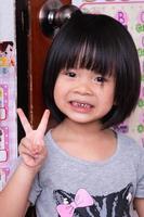 portrait jolie fille asiatique avec un doux sourire. un enfant heureux lève le doigt vers le signe v. les enfants ont 4 ans. image verticale. photo