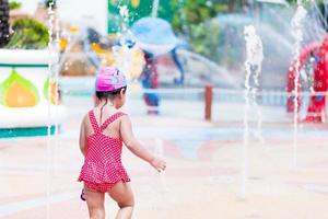 vue arrière noire. portrait de 3-4 ans. enfant asiatique fille jouant à la fontaine de la cour. à l'heure d'été. enfant portant un maillot de bain rouge. luminosité dans l'enfance. activités par temps chaud. copie espace photo