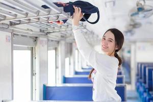 une belle femme asiatique en chemise blanche voyage en train le jour des vacances alors qu'elle tient un sac à garder sur l'étagère supérieure. photo