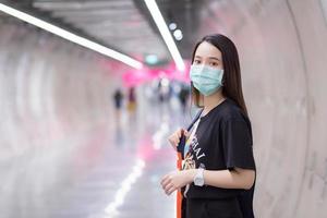 une belle femme asiatique porte une chemise noire et un masque médical pendant qu'elle entre dans le tunnel du métro. soins de santé, pollution pm2,5 et nouveau concept normal. photo