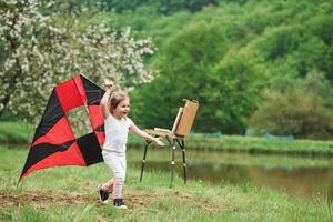 sentir la liberté. enfant de sexe féminin positif courant avec un cerf-volant de couleur rouge et noir dans les mains à l'extérieur photo