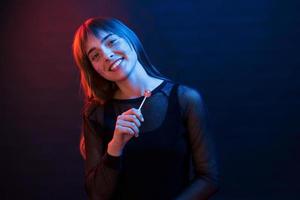 avec des bonbons roses à la main. studio tourné en studio sombre avec néon. portrait de jeune fille photo