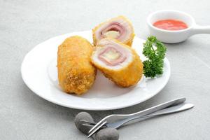 cordon bleu croustillant, rouleau de filet de poulet au jambon et fromage. servi dans une assiette blanche sur fond gris. photo