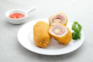 cordon bleu croustillant, rouleau de filet de poulet au jambon et fromage. servi dans une assiette blanche sur fond gris. photo