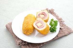 cordon bleu croustillant, rouleau de filet de poulet au jambon et fromage. servi dans une assiette blanche sur fond gris. photo