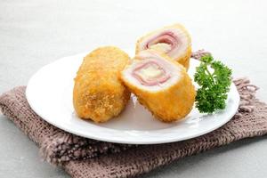 cordon bleu croustillant, rouleau de filet de poulet au jambon et fromage. servi dans une assiette blanche sur fond gris. photo