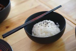 riz japonais avec sésami noir sur le dessus dans le bol noir et baguettes sur la table en bois. photo