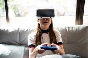 concept de technologie, de jeu, de divertissement et de personnes. femme asiatique profitant de lunettes de réalité virtuelle tout en se relaxant dans le salon. heureux jeune homme avec casque vr jouant au jeu vidéo à la maison photo