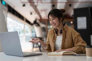 portrait d'une jeune femme asiatique utilisant un ordinateur portable et écrivant une liste de prise de notes dans le bloc-notes travaillant ou apprenant sur un ordinateur portable à l'intérieur - cours éducatif ou formation, séminaire, concept d'éducation en ligne. photo