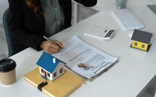 femme d'affaires asiatique signe un contrat derrière le modèle architectural de la maison - concept immobilier photo