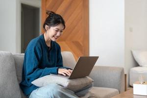 jeune femme asiatique utilisant un ordinateur portable dans le canapé avec un visage heureux debout et souriant avec un sourire confiant montrant les dents photo