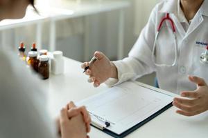 une femme médecin asiatique en uniforme médical blanc consulte une patiente dans un hôpital privé. femme thérapeute parle parler avec une cliente lors d'une consultation en clinique photo