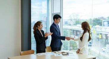 une femme d'affaires applaudit et félicite tandis que deux hommes d'affaires se serrent la main après avoir conclu un accord ou un accord. concept de travail et de réussite. photo