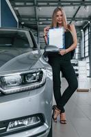 photographie verticale. fille et voiture moderne dans le salon. le jour à l'intérieur. achat d'un véhicule neuf photo