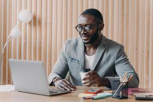 jeune entreprise afro-américaine souriante dans des verres assis avec une tasse de café sur le lieu de travail au bureau photo