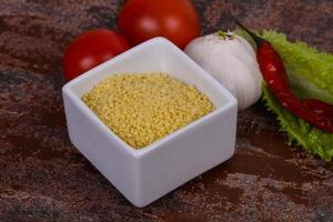 couscous cru dans le bol servi feuilles de salade, tomate et poivron photo