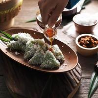 lupis, collation traditionnelle indonésienne à base de riz gluant, enveloppée de feuille de bananier, en forme de triangle servie avec du sucre de palme liquide et de la noix de coco râpée photo