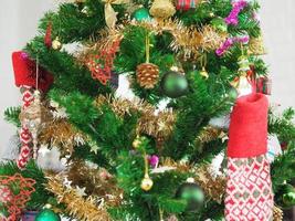 décorations de noël arbre vert suspendu, boîte cadeau dorée, boule verte, pommes de pin marron, chaussettes, chaussures, cloche rose enroulée autour d'elle avec un ruban d'or sur fond blanc photo