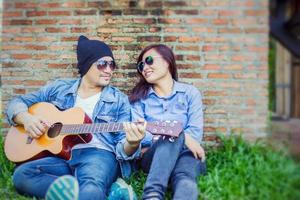 homme hipster jouant de la guitare pour sa petite amie en plein air contre un mur de briques, s'amusant ensemble. photo