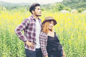 jeune couple hipster relaxant dans un champ de fleurs jaunes en été. profiter de la nature. photo