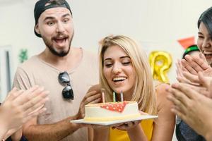 belle fille blonde américaine soufflant le gâteau d'anniversaire dans la fête avec des amis applaudir sa chanson de célébration d'anniversaire. photo