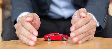 couverture de main d'homme d'affaires ou jouet de voiture rouge de protection sur la table. concept financier, monétaire, de refinancement et d'assurance automobile photo