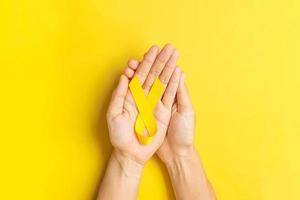 main tenant un ruban jaune sur fond jaune pour soutenir les personnes vivant et malades. journée de prévention du suicide en septembre, mois de sensibilisation au cancer infantile et concept de journée mondiale contre le cancer photo