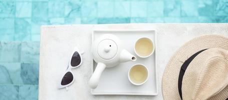 lunettes de soleil blanches, théière chaude et chapeau près de la piscine dans un hôtel de luxe. voyage d'été, vacances, vacances et concept de week-end