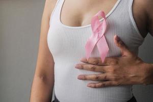 gros plan d'un ruban rose sur la poitrine de la femme pour soutenir le cancer du sein. concept de sensibilisation aux soins de santé et au cancer du sein. photo