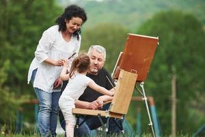 donne-moi ce pinceau. grand-mère et grand-père s'amusent dehors avec sa petite-fille. conception de la peinture photo