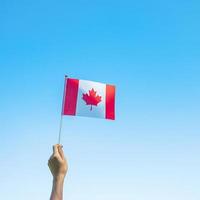 main tenant le drapeau du canada sur fond de ciel bleu. concepts de la fête du canada et de la fête du canada photo