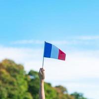 main tenant le drapeau de la france sur fond de ciel bleu. vacances de la fête nationale française, du jour de la bastille et des concepts de célébration heureuse photo