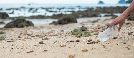 la main bénévole ramasse les ordures, les ordures de bouteilles en plastique sur la plage. concept d'écologie, d'environnement, de pollution et de problème écologique photo