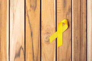 ruban jaune sur fond de table en bois pour soutenir les personnes vivant et malades. journée de prévention du suicide en septembre, mois de sensibilisation au cancer infantile et concept de journée mondiale contre le cancer photo