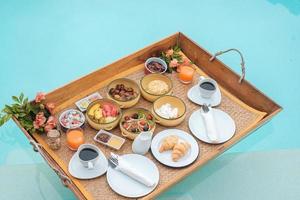 plateau de petit-déjeuner flottant dans la piscine d'un hôtel de luxe ou d'une villa tropicale, fruits, croissant, café et jus d'orange. été exotique, détente, voyage tropical et concept de vacances photo