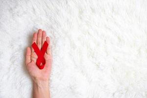 main tenant un ruban rouge pour soutenir les personnes vivant et malades. concept de soins de santé et de rapports sexuels protégés. décembre journée mondiale du sida et mois de sensibilisation au cancer du myélome multiple photo