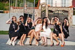 groupe de 7 filles portant du noir et 2 mariées assises sur un banc et s'amusant à la fête de poule. photo