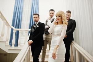 trois hommes barbus élégants bien habillés avec une fille blonde en robe blanche posée. groupe de musiciens ou chanteurs. photo