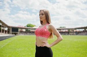 fitness fille sportive en tenue de sport dans un stade de football sports de plein air. séance d'entraînement de femme sexy heureuse sur le fond de l'herbe verte. photo