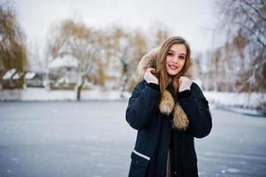 belle fille brune en vêtements chauds d'hiver. modèle sur la veste d'hiver contre le lac gelé au parc. photo