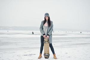 fille brune élégante en casquette grise, style de rue décontracté avec planche à roulettes le jour de l'hiver. photo